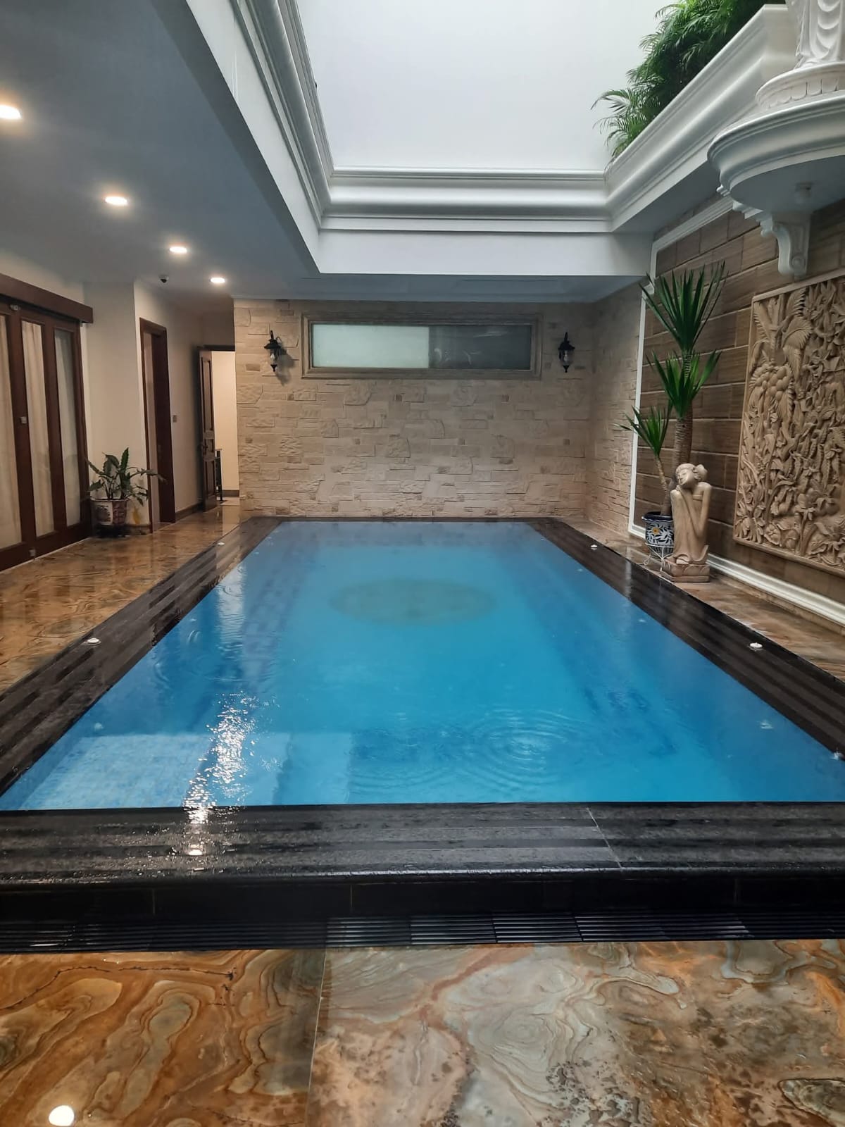 Kolam renang indoor mewah dengan finishing batu alam dan patung dekoratif